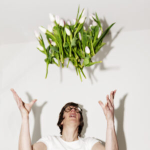 En person kastar upp en stor bukett tulpaner i luften mot vit bakgrund. 
